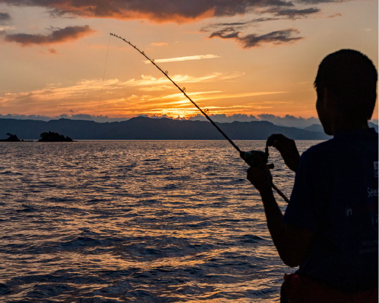 夕日の海で釣り糸を垂らす参加者のシルエット