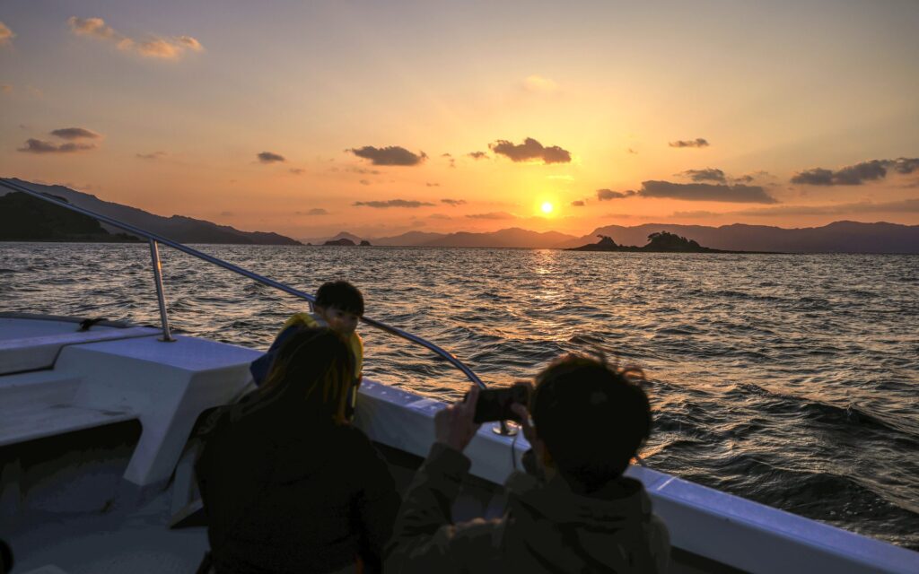 海上タクシーの船上で、夕日と島影を眺める参加者